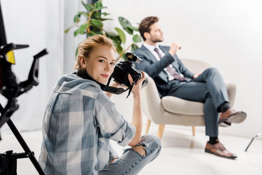 young female photographer smiling at camera while photographing handsome businessman in studio